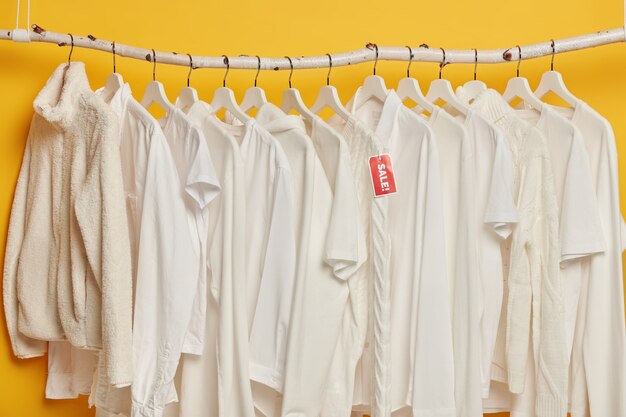 黄色の背景で隔離のハンガーに白い服のクリアランスセール。女性のためのファッション衣類の選択。