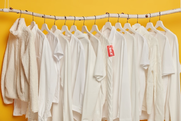 Распродажа белой одежды на вешалках, изолированных на желтом фоне. Подбор модной одежды для женщин.