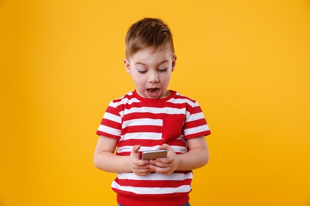 Clever excited little boy reading message on mobile phone