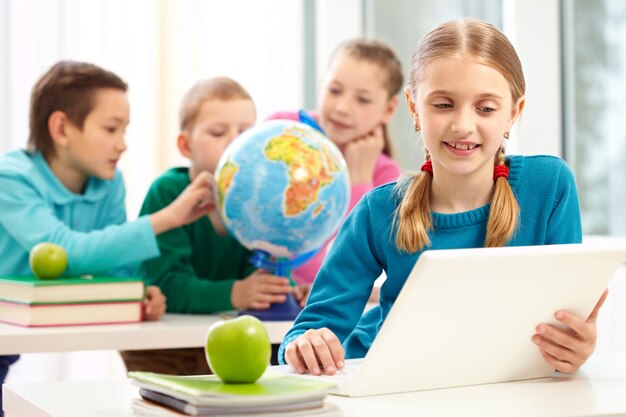 Clever schoolgirl with laptop in class