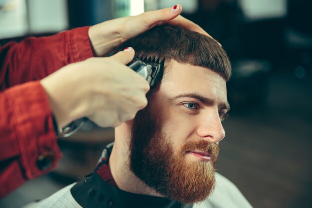 Client during beard shaving in barbershop. Female barber at salon. Gender equality. Woman in the male profession. Hands close up