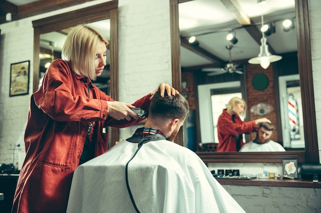 Client during beard shaving in barbershop. Female barber at salon. Gender equality. Woman in the male profession.