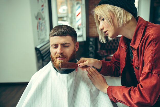 Client during beard shaving in barbershop. Female barber at salon. Gender equality. Woman in the male profession.