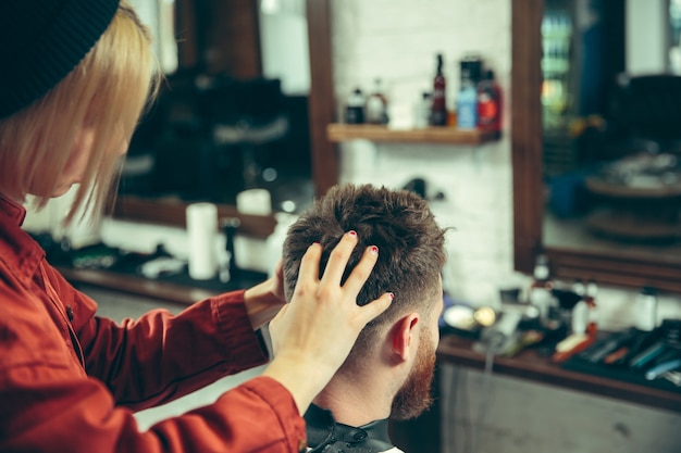 Client during beard shaving in barbershop. Female barber at salon. Gender equality. Woman in the male profession.