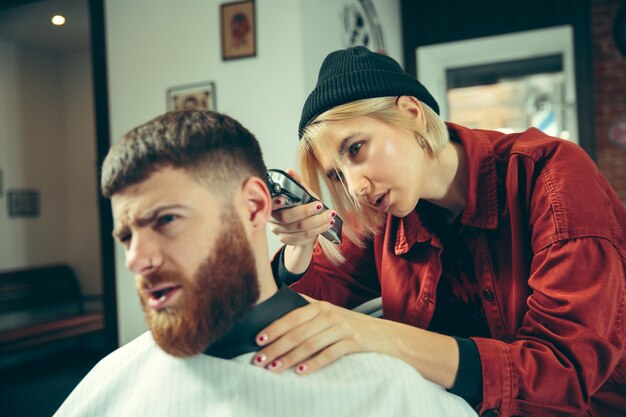 Client during beard shaving in barbershop. Female barber at salon. Gender equality. Woman in the male profession.