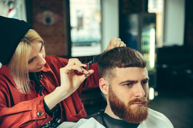 理髪店でひげを剃っている間のクライアント。サロンの女性理髪店。男女平等。男性の職業の女性。