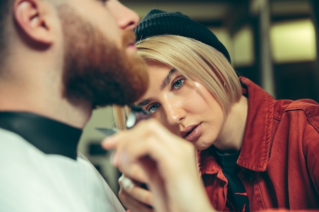 Client during beard shaving in barbershop. Female barber at salon. Gender equality. Woman in the male profession.