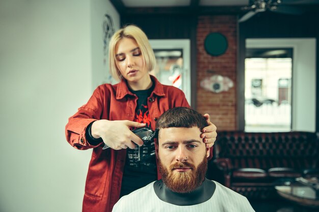 Client during beard shaving in barbershop. Female barber at salon. Gender equality. Woman in the male profession.