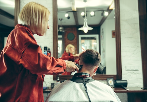 Client during beard shaving in barbershop. Female barber at salon. Gender equality. Woman in the male profession.