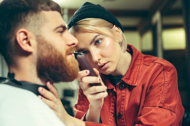 Client during beard shaving in barbershop. Female barber at salon. Gender equality. Woman in the male profession.