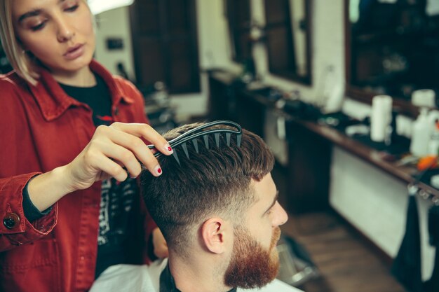 Client during beard shaving in barbershop. Female barber at salon. Gender equality. Woman in the male profession.