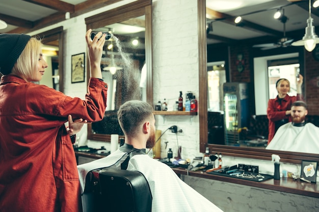 Client during beard shaving in barbershop. Female barber at salon. Gender equality. Woman in the male profession.