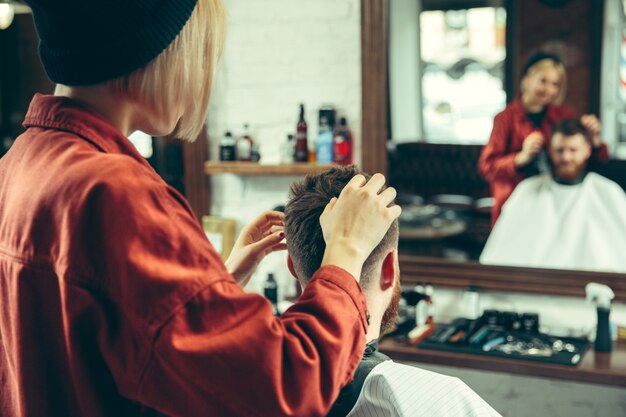 Client during beard shaving in barbershop. Female barber at salon. Gender equality. Woman in the male profession.