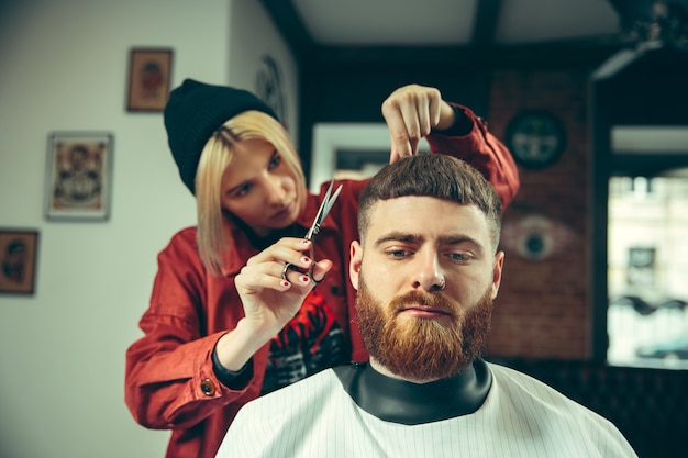Клиент во время бритья бороды в парикмахерской. Женский парикмахер в салоне. Гендерное равенство