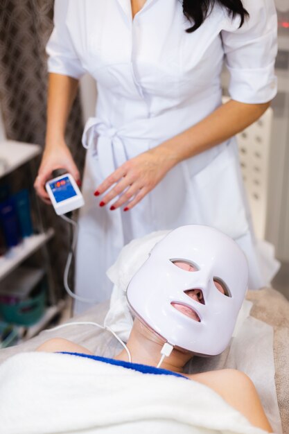 Клиентка лежит в салоне на косметологическом столе с белой маской на лице.