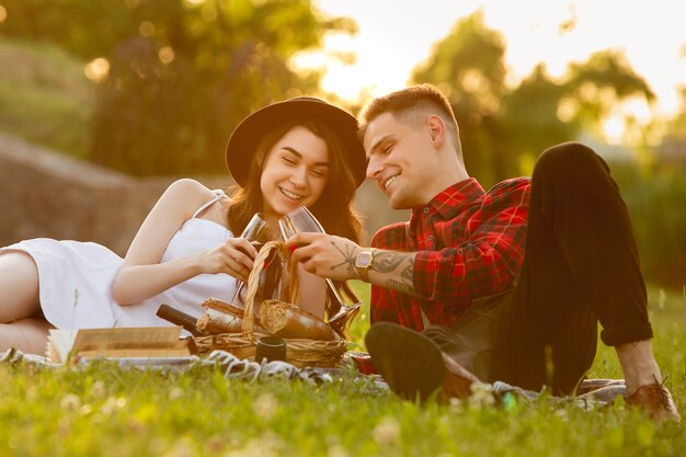 Clinking glasses with wine. Caucasian young couple enjoying weekend in the park on summer day