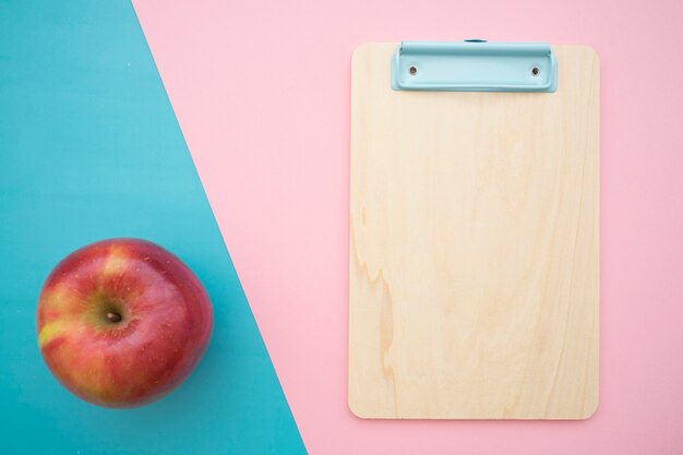 Clipboard and apple on blue and pink background