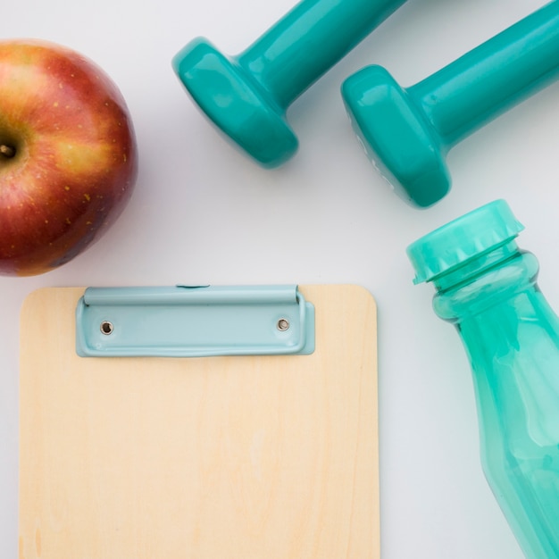 Clipboard, apple, bottle and dumbbells close up