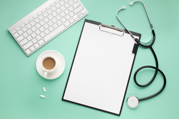 Clipboard; wireless keyboard; cup of coffee and stethoscope on green desk