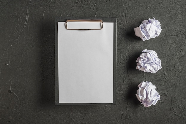 Clipboard with blank paper besides crumpled papers in a row