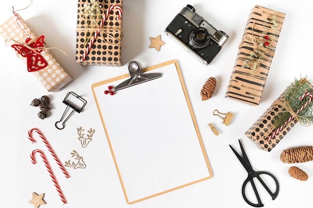 Clipboard with gift boxes and camera on white table