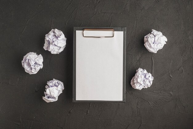 Clipboard with paper surrounded by crumpled papers on black backdrop
