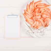 Free photo clipboard with prawn dish on kitchen table