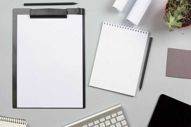 Clipboard with spiral notepad; pencil and keyboard on gray background