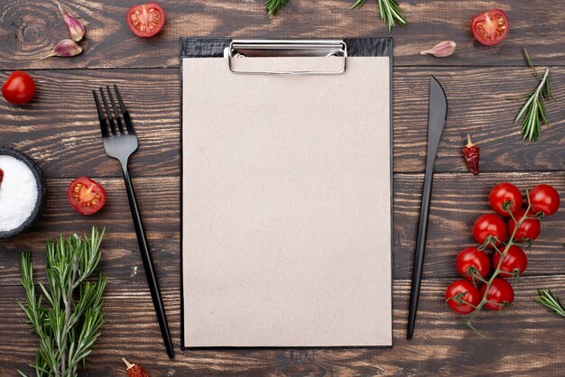 Clipboard with tomatoes and cutlery on table