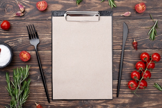 Clipboard with tomatoes and cutlery on table