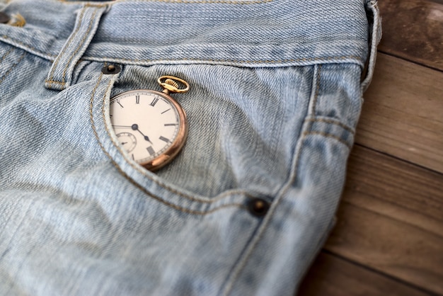 木製の表面-時間管理の概念のジーンズのポケットの時計