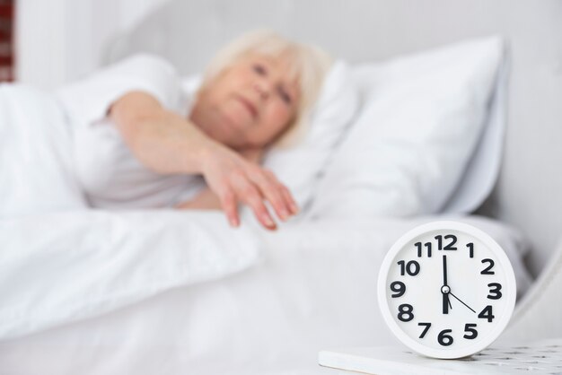 Clock and sleeping elder woman on background