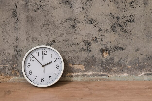 Clock on wooden desk against weathered wall