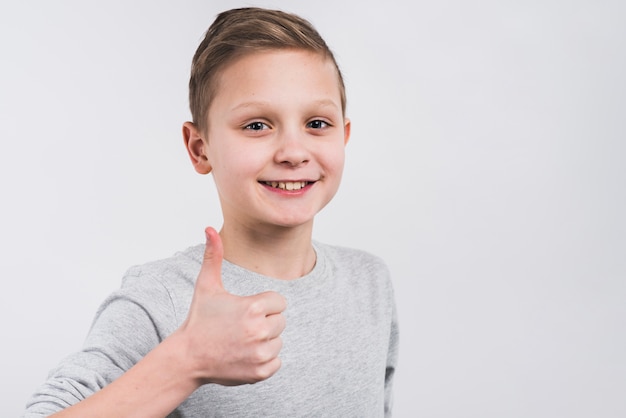 Clos-up of a smiling boy showing thumb up sign standing against grey background