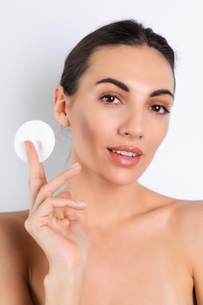 Close beauty portrait of a topless woman with perfect skin and natural makeup removing cotton pads on a white backgroundx9