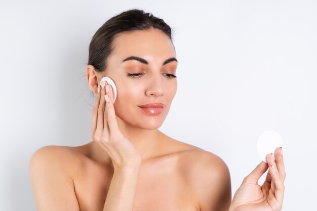 Close beauty portrait of a topless woman with perfect skin and natural makeup removing cotton pads on a white backgroundx9