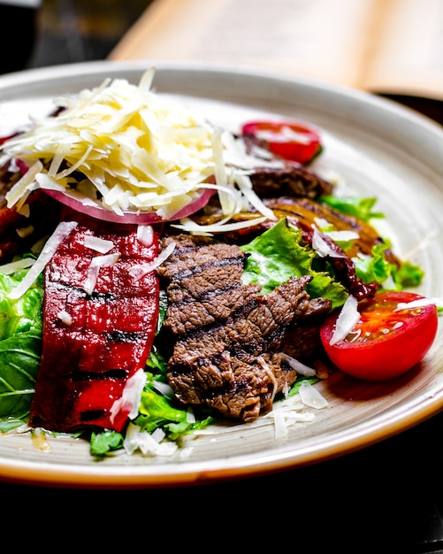 Close front view grilled meat with vegetables and lettuce with grated cheese on a plate