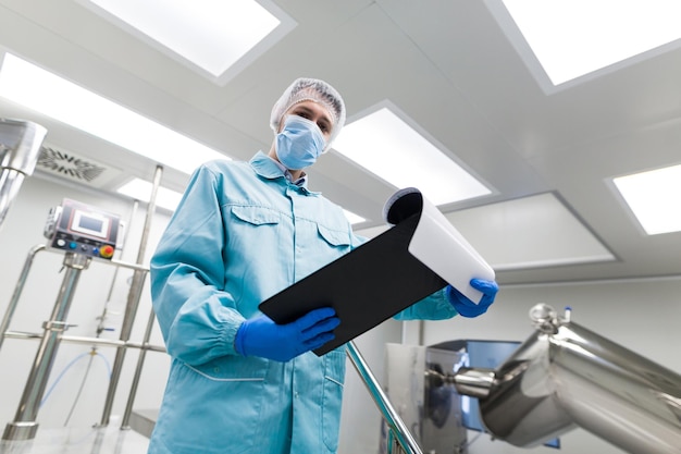Близкий взгляд ученого в синем лабораторном костюме стоит на металлической хромированной лестнице в лаборатории и смотрит в планшет снизу