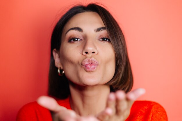 Close portrait of woman on red wall looks to front and sends air kiss