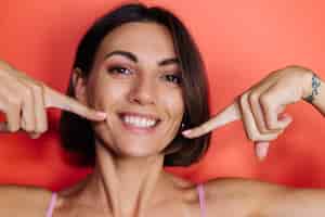 Free photo close portrait of woman on red wall shows points fingers on white teeth smile