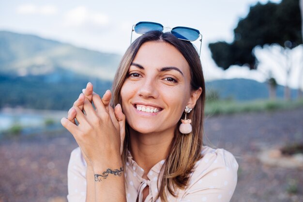 Close portrait of young woman with sunglasses and earrings at warm sunset in park