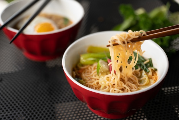 Close shot of chopsticks with noodles near the soup with blurred background