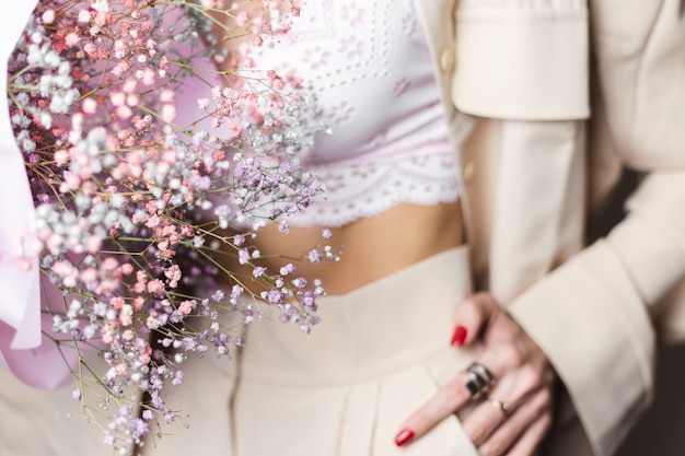 베이지 색 양복과 흰색 브래지어에 가까운 총 머리 여자가 손가락에 다채로운 말린 꽃 빨간 매니큐어 두 반지의 꽃다발을 개최