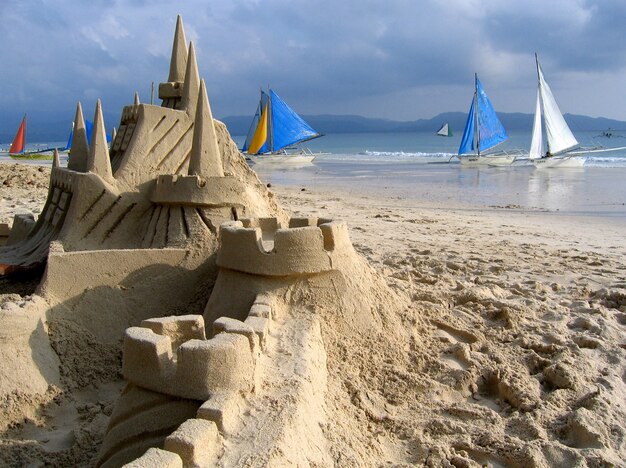 Close shot of a sandcastle on a beach shore with boats in the background