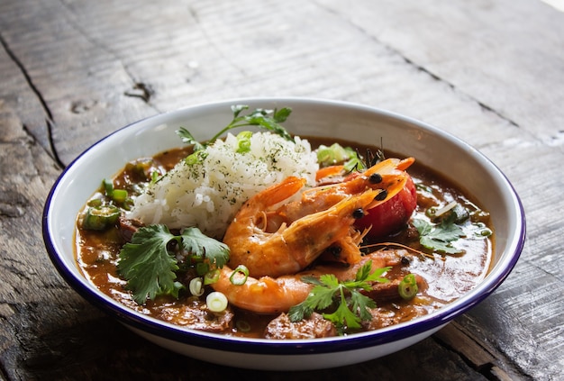 Close shot of soup with shrimps, rice, and vegetables leaves in a bowl on a wooden surface