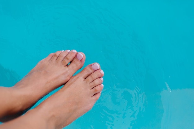 Esposizione ravvicinata dei piedi della donna con smalto gel per pedicure francese su sfondo di acqua blu in piscina.