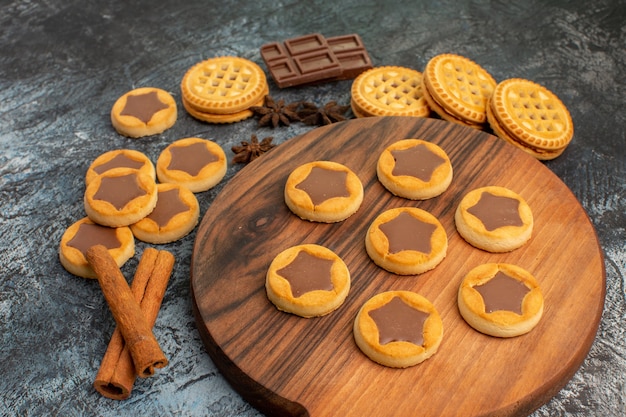 Закройте боковую съемку печенья на деревянном блюде и корицы и шоколадных конфет на сером