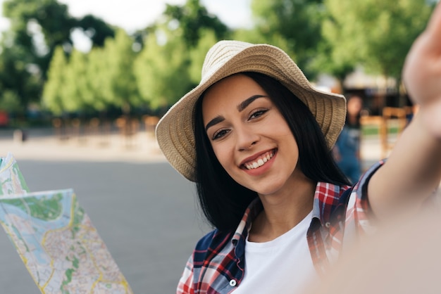 Close-u of smiling woman holding map and taking selfie at outdoors