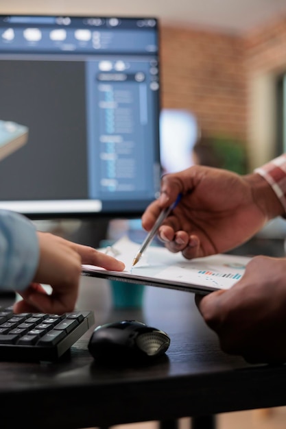 Close up of 3D digital artists reviewing sketch scene plan and simulated render times, Creative industry enthusiasts with CAD open in background discussing technical issues while pointing at clipboard