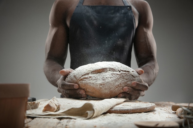 Крупным планом афро-американский мужчина готовит свежие хлопья, хлеб, отруби на деревянном столе. Вкусная еда, питание, крафтовый продукт. Безглютеновая пища, здоровый образ жизни, экологически чистое и безопасное производство. Ручной работы.